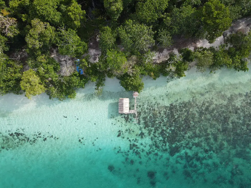 Aerial view of overwater hut and turquoise reef Raja Ampat